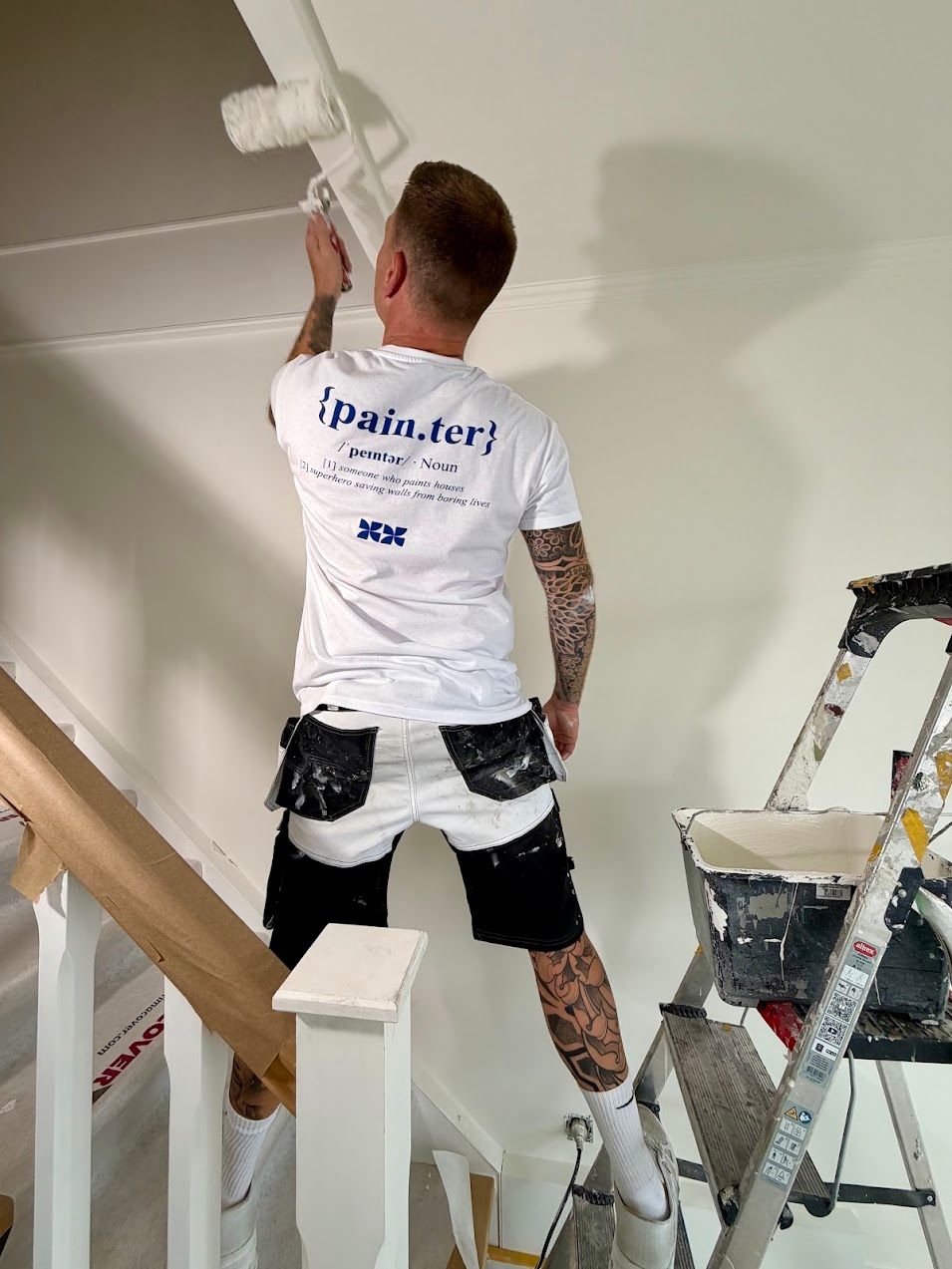 Lorenzo Berckmoes schildert een plafond boven de trap met de roller, trap en leuning volledig afgedekt
